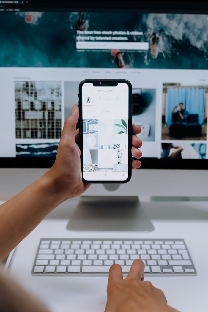 Person uses a smartphone in front of a computer screen displaying stock photos, showcasing modern technology use.